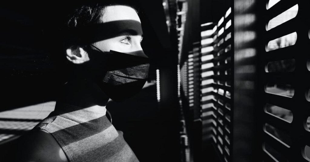 A woman looking at the window in fear. Unsure of outside.